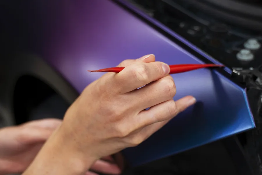 Folie wird mit dem Rakel über die Kante eines blau-violett folierten Fahrzeugs gezogen